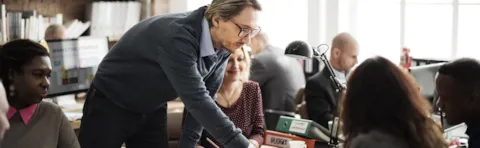 Man legt iets uit aan een groep collega's, met papieren ter ondersteuning die op tafel liggen.