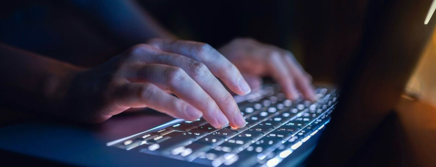 Woman's hand typing on computer keyboard in the dark