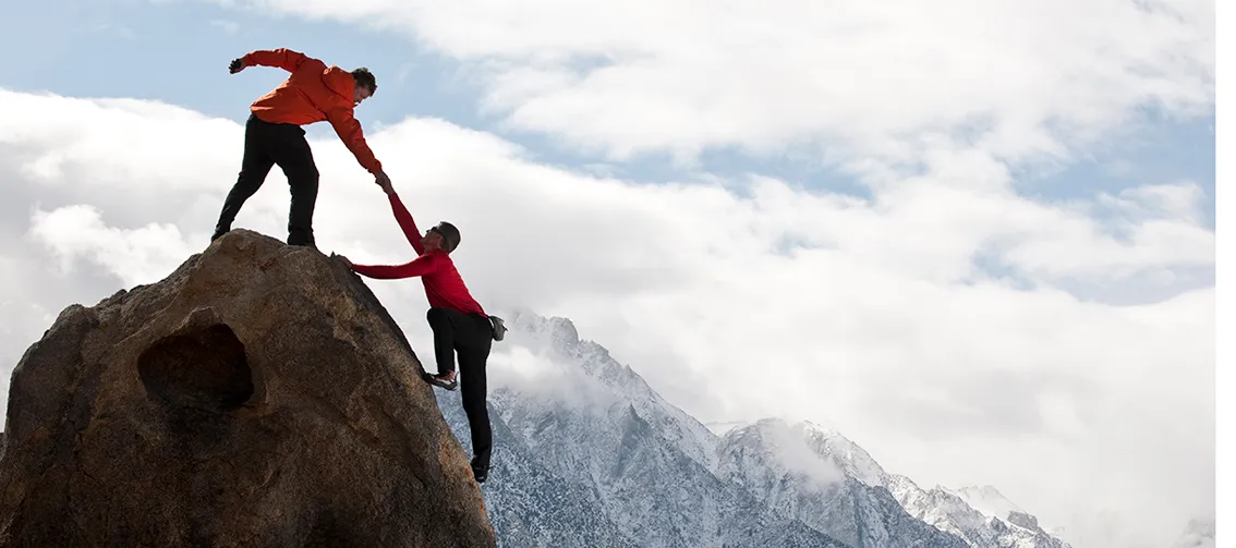 Mountaineer giving helping hand to colleague reaching top of mountain